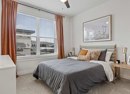 A bedroom with a large bed and a window with brown curtains.