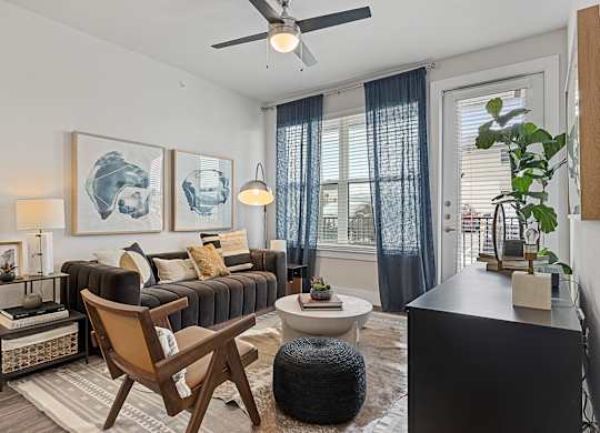 A living room with a black couch, a brown chair, and a ceiling fan.