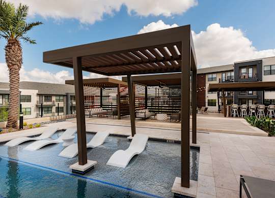 A pool area with a sun shade and a palm tree.