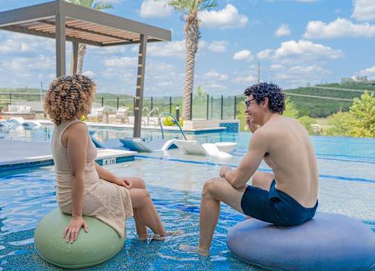 A man and a woman are sitting on pool floats and talking.