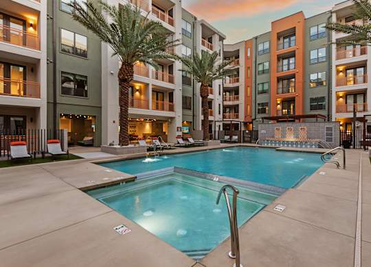 A swimming pool in front of apartment buildings with palm trees.