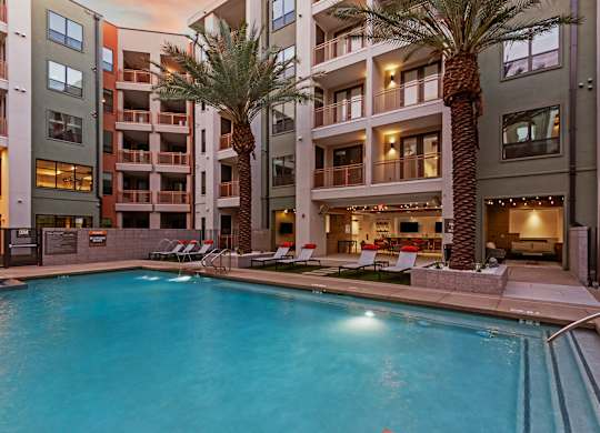A swimming pool in front of a building with palm trees.