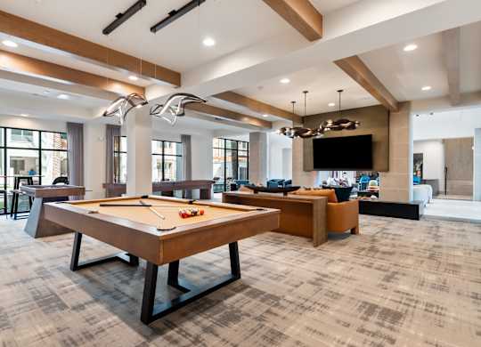 A billiard table is in the middle of a room with a bar and a television.