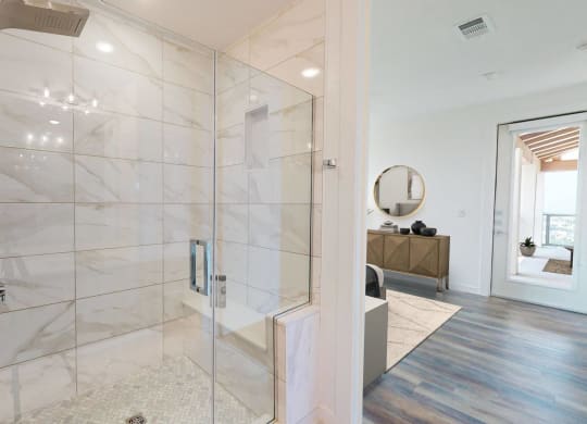 the master bathroom has a large shower with marble tiles and a wood floor