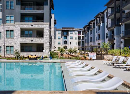 an outdoor pool with white chairs and an apartment building in the background
