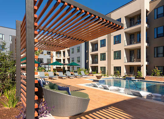 a large pool with chairs and umbrellas in front of an apartment building