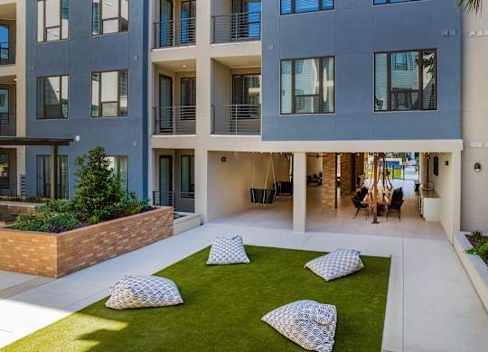 an open courtyard with pillows and grass in front of an apartment building