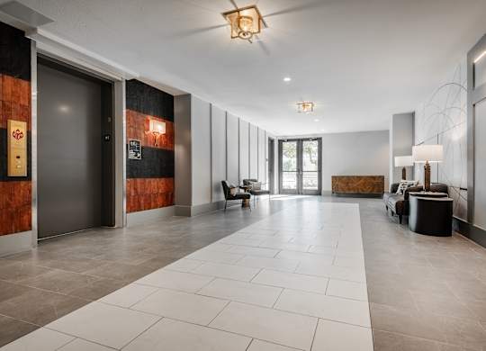 the lobby of a condo with a large white tiled floor and a glass door