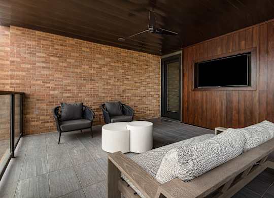 a large covered patio with a brick wall and a wooden patio table with two chairs and a