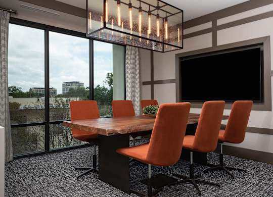 a conference room with a large screen tv and a wooden table with orange chairs