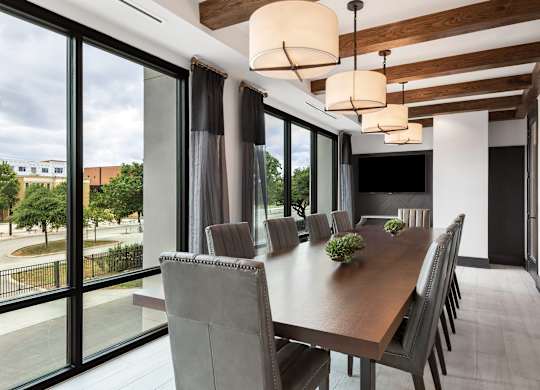 a long dining table with chairs and a television in a room with large windows