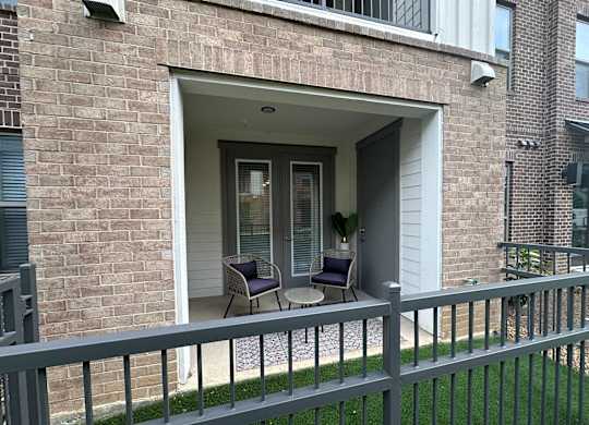 A patio with a table and two chairs is in front of a brick building.