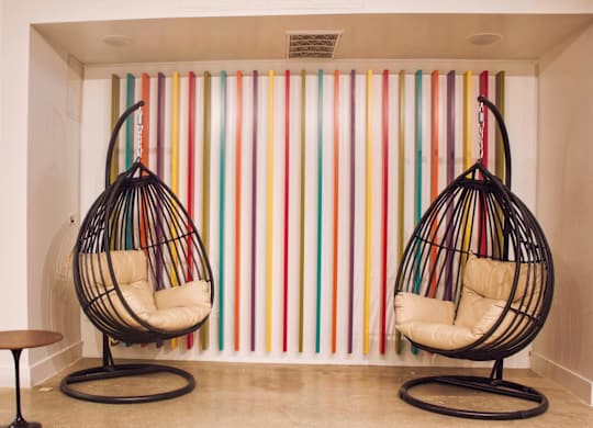 Two hanging chairs in front of a colorful striped wall.