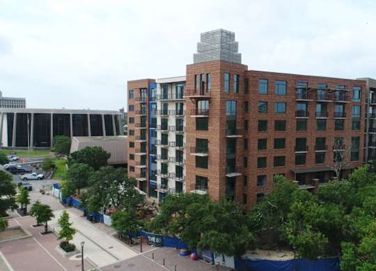 A large red brick building with a glass facade is surrounded by trees.