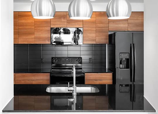 Modern kitchen with wood cabinetry and black backsplash at THE'68 Apartments, San Antonio, Texas