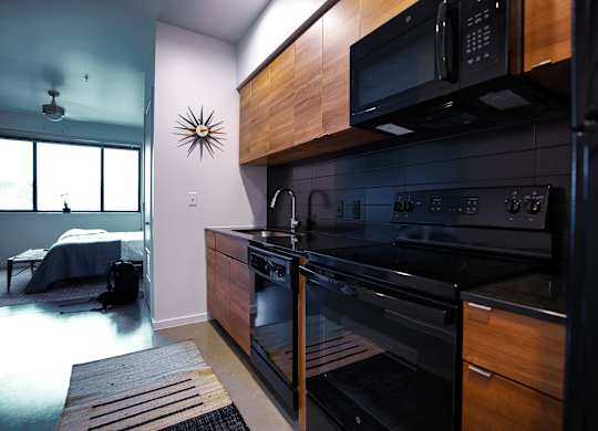 Contemporary kitchen with black appliances and wood finishes at THE'68 Apartments, San Antonio