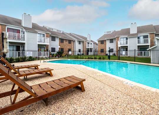 a swimming pool with two wooden benches next to an apartment building at Northchase, Austin, TX