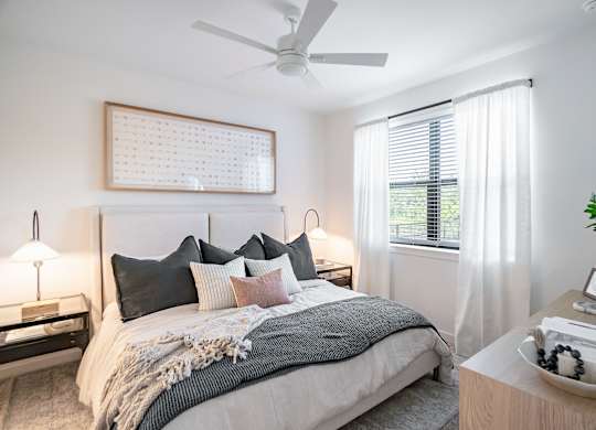 A bedroom with a bed, nightstand, and a plant.