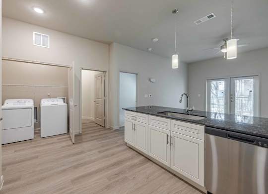 Kitchen with laundry room and dark countertops at Emilia Apartments, Boerne, TX