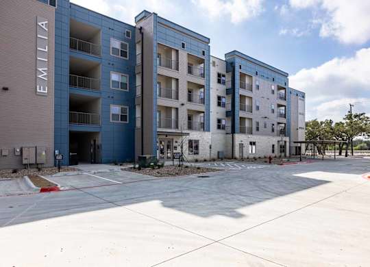 Modern apartment building exterior with parking area at Emilia Apartments, Texas