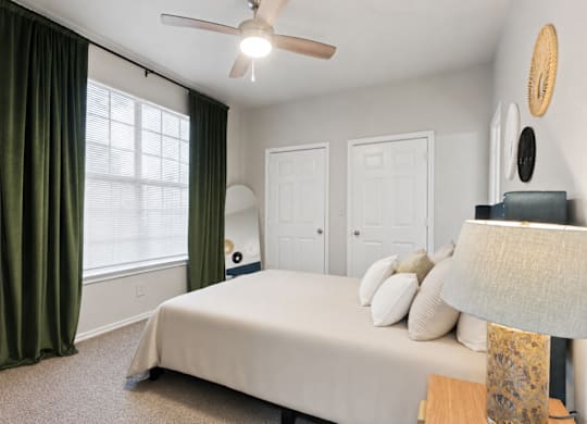 A bedroom with a bed, a ceiling fan, and a window with green curtains.