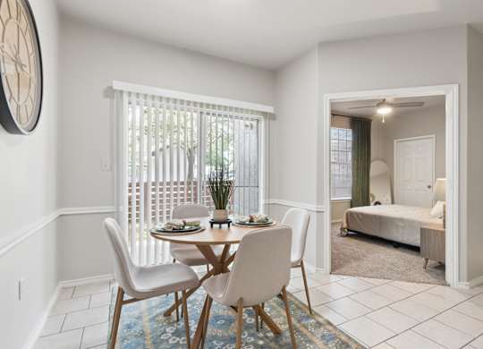 A dining room with a table set for two and a bedroom in the background.