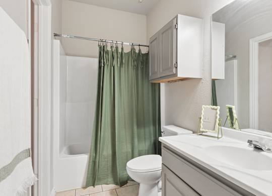 A bathroom with a white toilet, a green shower curtain, and a white sink.