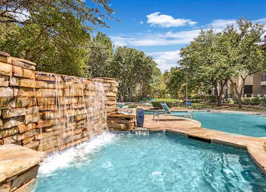 A pool with a waterfall and a stone wall.