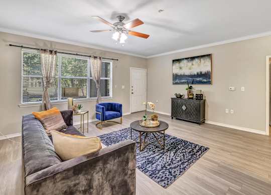 A living room with a brown couch, a blue chair, a coffee table, and a ceiling fan.