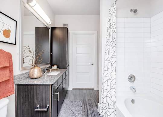 Bathroom with dark vanity and white tile shower at Sienna at Westover Hills Apartments, San Antonio