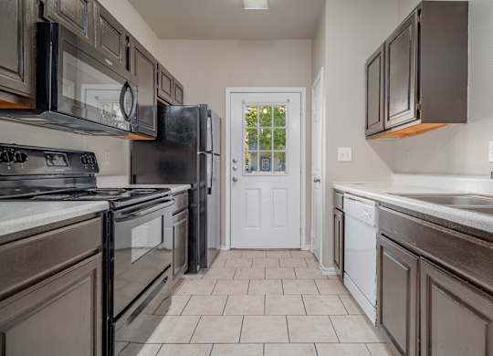 Galley kitchen with white appliances and tile flooring at Houston Street Townhomes Apartments, San Antonio, TX 78220