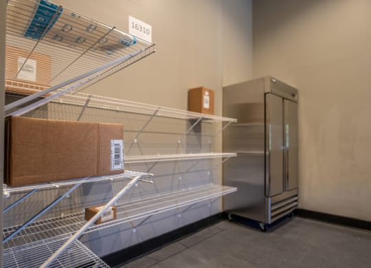 a room with a wire shelving unit with boxes on it and a refrigerator in the background