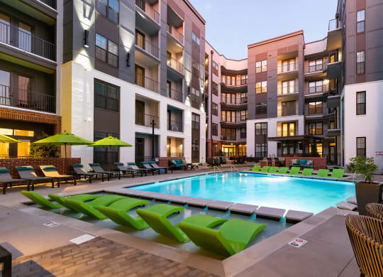 a swimming pool with green lounge chairs and umbrellas in front of an apartment buildingat Abberly Foundry Apartment Homes, Nashville