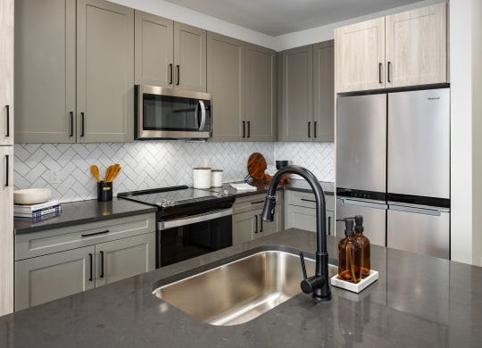 a kitchen with gray cabinets and a stainless steel sink at Abberly Foundry Apartment Homes, Nashville, Tennessee