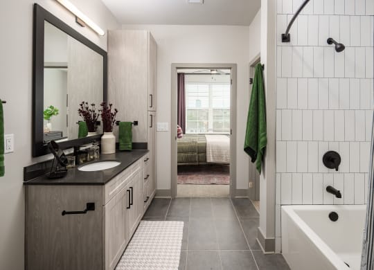 a bathroom with white tile walls and a black countertop with a sink and a bathtub at Abberly Foundry Apartment Homes, Nashville, 37203