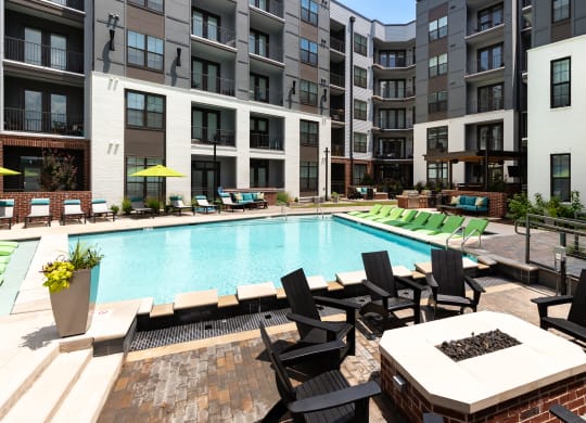 an outdoor swimming pool with lounge chairs and a fire pit in front of an apartment building at Abberly Foundry Apartment Homes, Nashville, 37203