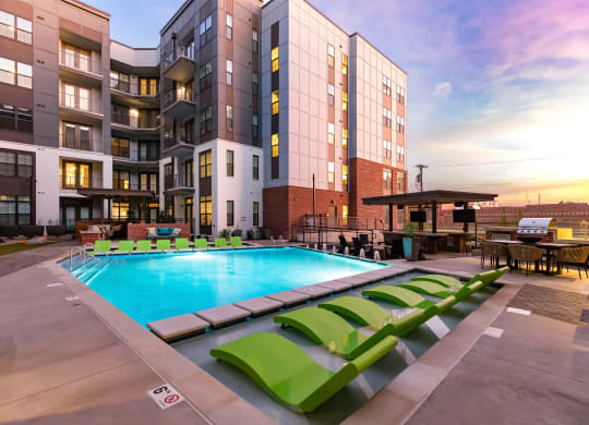 a swimming pool with green lounge chairs in front of an apartment building at Abberly Foundry Apartment Homes, Nashville, TN