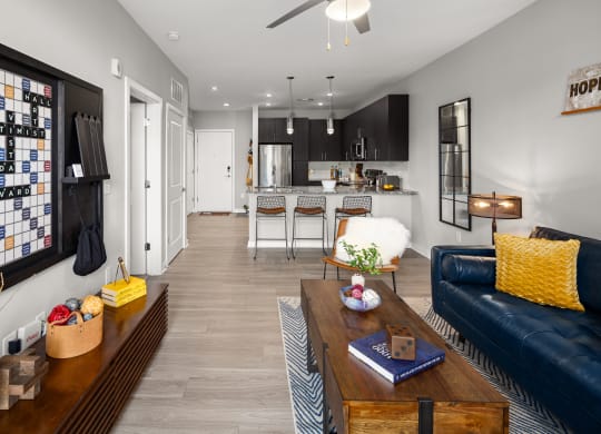 a living room with a blue couch and coffee table and a kitchen in the background  at Abberly Noda Vista Apartment Homes, North Carolina