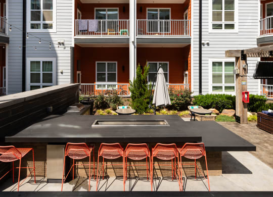 an outdoor kitchen with a bar and stools in front of an apartment building  at Abberly Noda Vista Apartment Homes, North Carolina, 28206