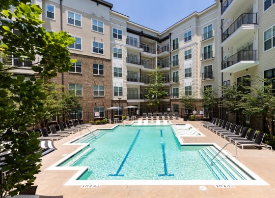 an outdoor swimming pool with chaise lounge chairs and an apartment building in the background at Abberly Onyx Apartment Homes, Decatur, Georgia