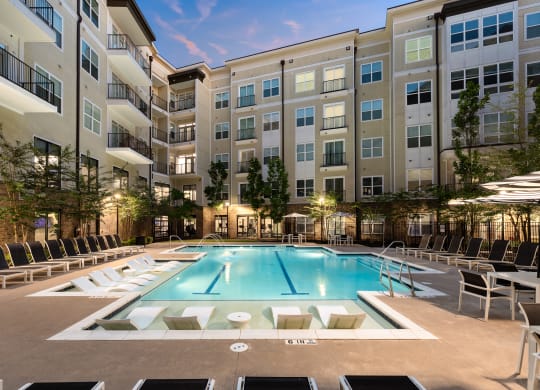 a pool with lounge chairs and umbrellas in front of an apartment building  at Abberly Onyx Apartment Homes, Decatur, 30033