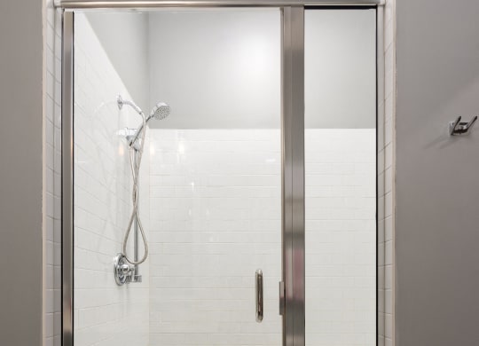the shower in the master bathroom has a glass door and white tiles