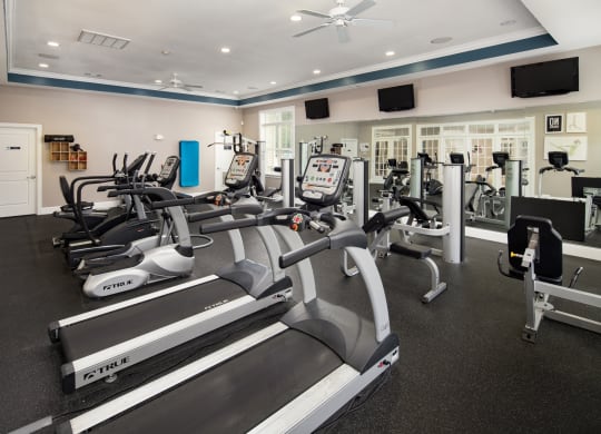 a gym with cardio equipment and televisions on the wall