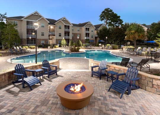 a swimming pool with a fire pit and chairs with an apartment building in the background