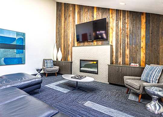 A modern living room with a grey sofa, a grey armchair, a white coffee table, a TV on the wall, and a wooden wall paneling.