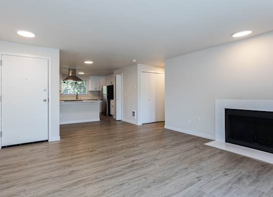 A white interior with a fireplace and a kitchen in the background.