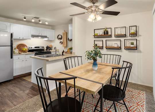 A kitchen with a table and chairs in the foreground and a fridge, stove, and oven in the background.