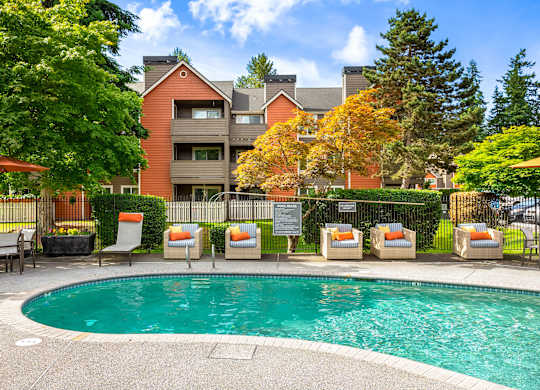 A pool surrounded by orange chairs and a building in the background.