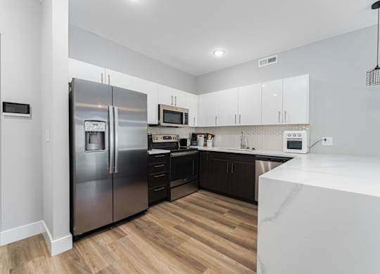 A modern kitchen with a stainless steel refrigerator and wooden flooring.