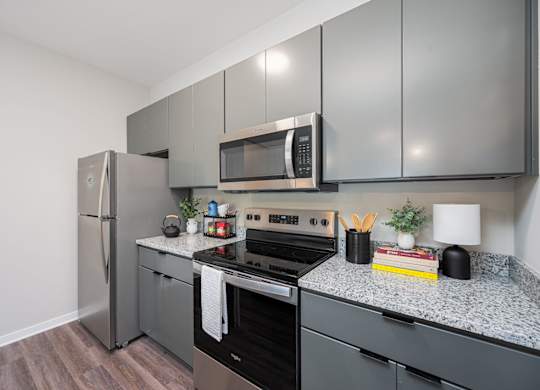 A kitchen with a refrigerator, microwave, oven, and countertop with a plant and a book on it.